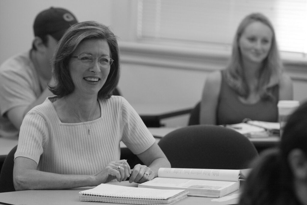 A woman sits with an open book and notebook in class.
