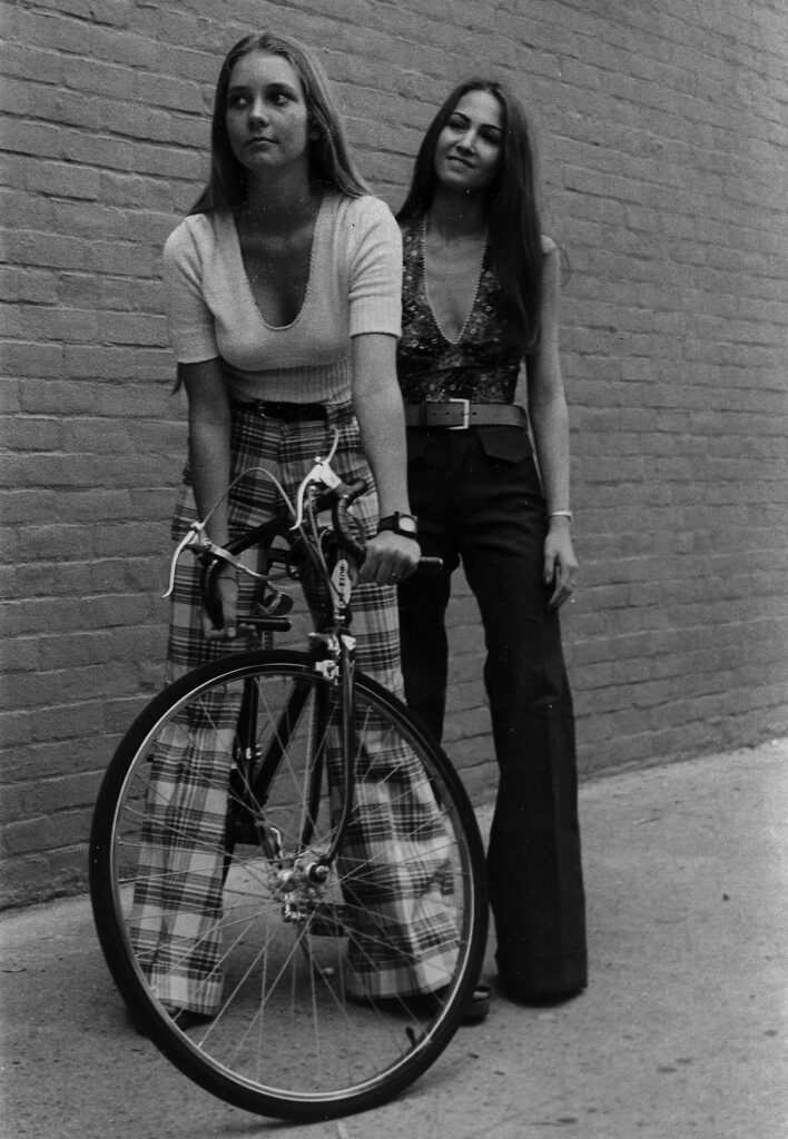 Two girls wear bellbottoms and slim fit shirts in the 1970s.