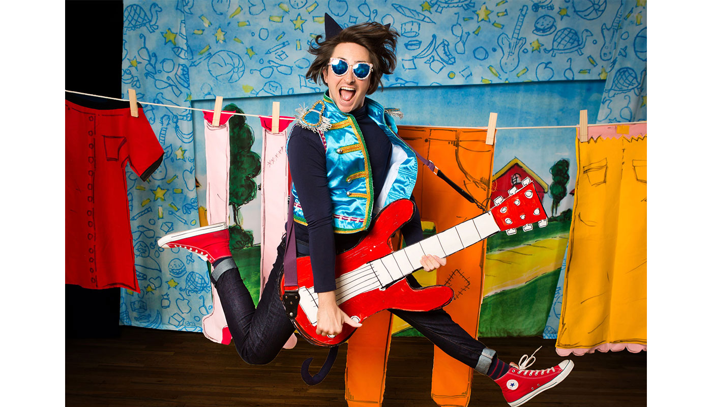 pete the cat. someone holding a guitar jumping in the air with their legs kicked out wearing cat ears