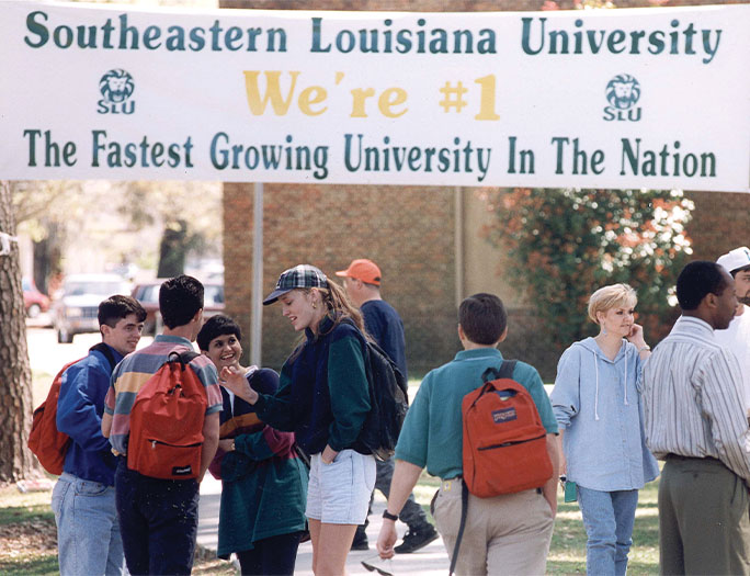 Students under sign reading Southeastern Louisiana University - The Fastest Growing University In The Nation.