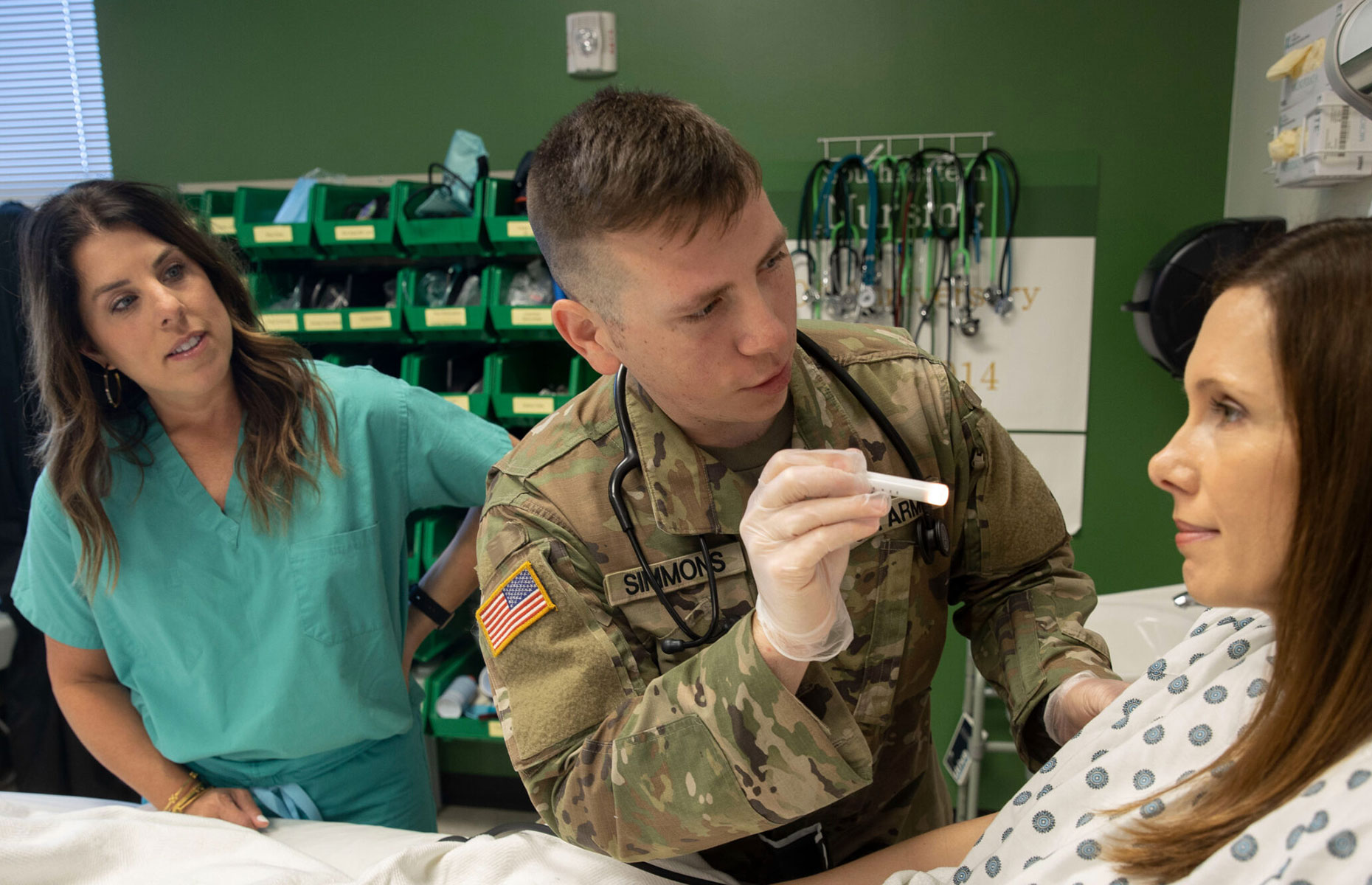 Military student checking the eyes of a patient inside a nursing room.